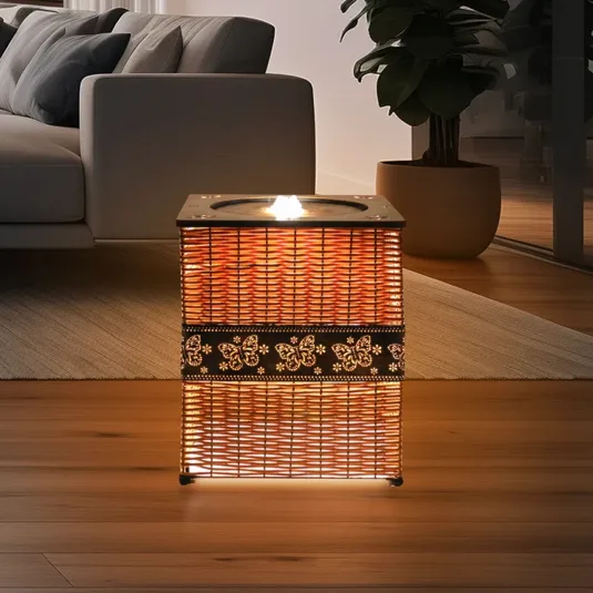 A woven rectangular lamp with floral patterns emits a warm glow, placed in a modern living room setting with a sofa, rug, and potted plant.