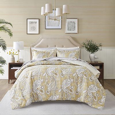 A paisley-patterned king-size comforter set in shades of gold and white, comprising a comforter, shams, and decorative pillows, displayed on a bed with a matching headboard.