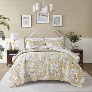 A paisley-patterned king-size comforter set in shades of gold and white, comprising a comforter, shams, and decorative pillows, displayed on a bed with a matching headboard.