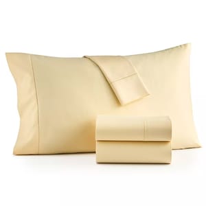 A set of cream-colored bed linens is displayed, including a pillowcase, flat sheet, and fitted sheet.