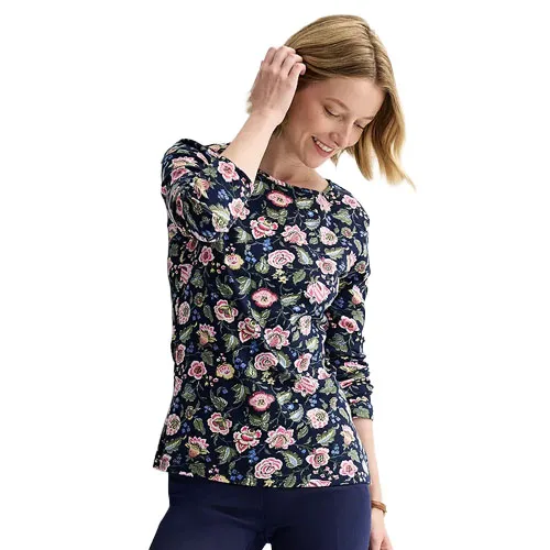 A woman is wearing a long-sleeved, floral-patterned top with a navy background, paired with dark pants.