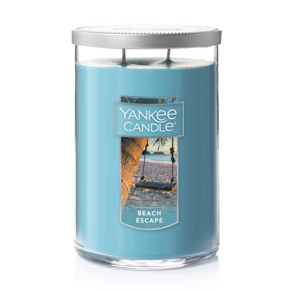 Blue Yankee Candle labeled \“Beach Escape\“ with a silver lid, showing a beach scene with a swing.
