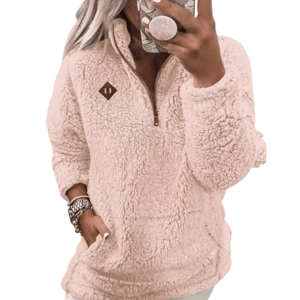 A person is wearing a pink sherpa fleece pullover with a quarter-zip design. The pullover has a brown patch on the chest, and the person has one hand in the pocket while taking a mirror selfie.