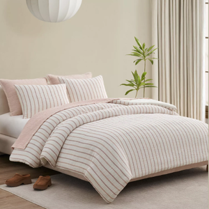 A neatly made bed features striped bedding in soft tones, complemented by matching pillows. The room includes a round pendant light, a potted plant, beige curtains, and brown shoes on a light rug.