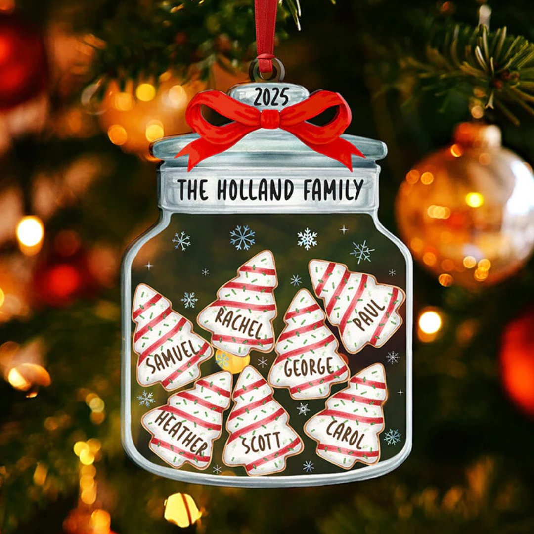 A Christmas ornament shaped like a jar with a red bow labeled \“The Holland Family 2025,\“ featuring cookie-shaped decorations with names: Samuel, Rachel, Paul, Heather, George, Scott, and Carol. It's hanging on a decorated Christmas tree.