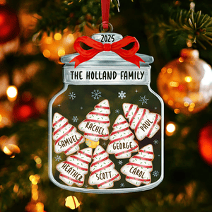 A Christmas ornament shaped like a jar with a red bow labeled \“The Holland Family 2025,\“ featuring cookie-shaped decorations with names: Samuel, Rachel, Paul, Heather, George, Scott, and Carol. It's hanging on a decorated Christmas tree.