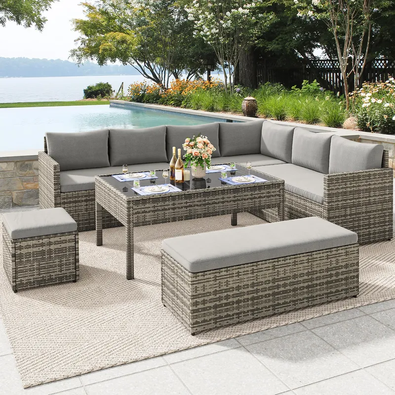 Outdoor patio set with a wicker design, featuring a sectional sofa with gray cushions, a rectangular table, and two ottomans, set on a textured rug near a poolside.