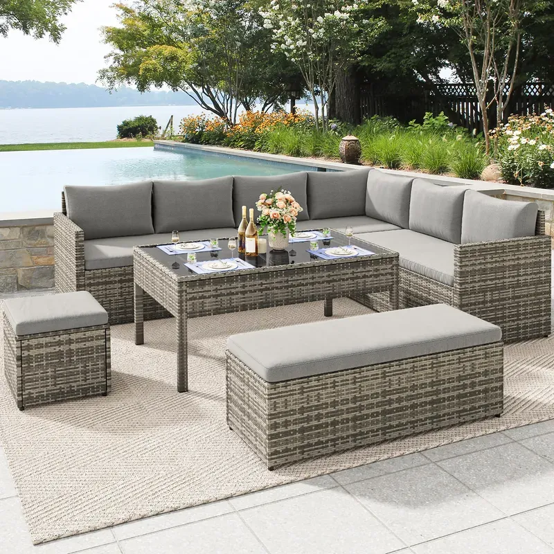 Outdoor patio set with a wicker design, featuring a sectional sofa with gray cushions, a rectangular table, and two ottomans, set on a textured rug near a poolside.