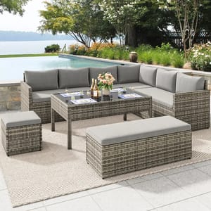 Outdoor patio set with a wicker design, featuring a sectional sofa with gray cushions, a rectangular table, and two ottomans, set on a textured rug near a poolside.