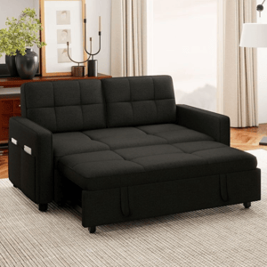 A black convertible sofa bed with a tufted design is shown, featuring a storage pocket on the armrest. The setting includes light-colored curtains, a rug, and a side table with decor items like plants and candlesticks.