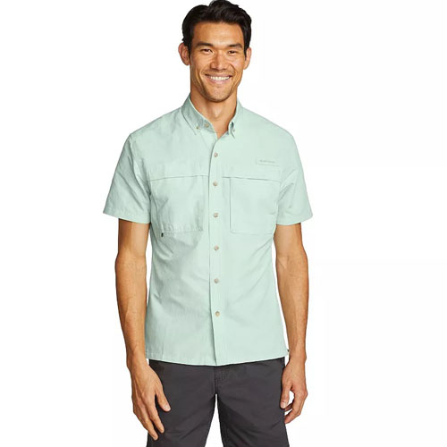 A man is wearing a light mint green, short-sleeve button-up shirt with two chest pockets, paired with dark pants.