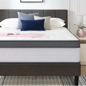 A modern bedroom setup features a bed with a plush mattress, several decorative pillows, and minimalistic bedside tables with lamps. A simple abstract painting adorns the wall above.