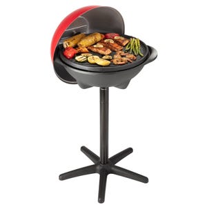 A Cuisinart electric grill with a stand features a circular cooking surface, grilling various foods like vegetables and meats. It has a red-lidded cover and a stable, star-shaped base.