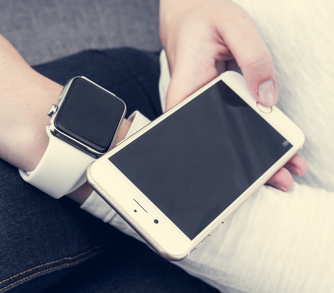 A smartwatch on a wrist next to a hand holding a smartphone.