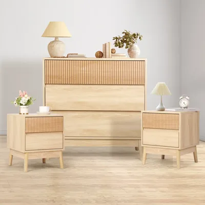 A minimalist furniture set with a tall dresser and two side tables in light wood, featuring grooved accents. Accessories include lamps, books, and decorative items.