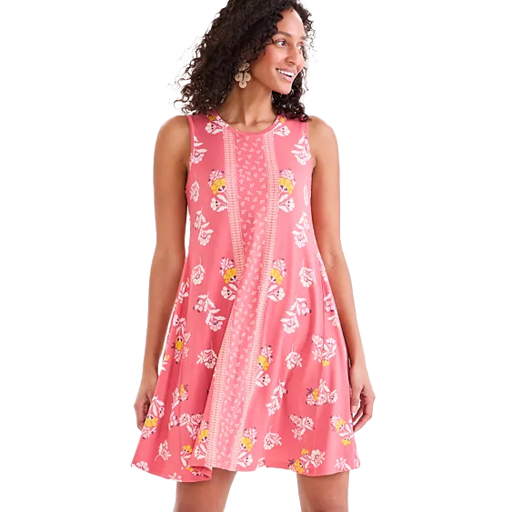 A woman is wearing a sleeveless pink floral dress with a decorative central panel and white and yellow floral patterns. She is accessorizing with large earrings.