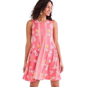 A woman is wearing a sleeveless pink floral dress with a decorative central panel and white and yellow floral patterns. She is accessorizing with large earrings.