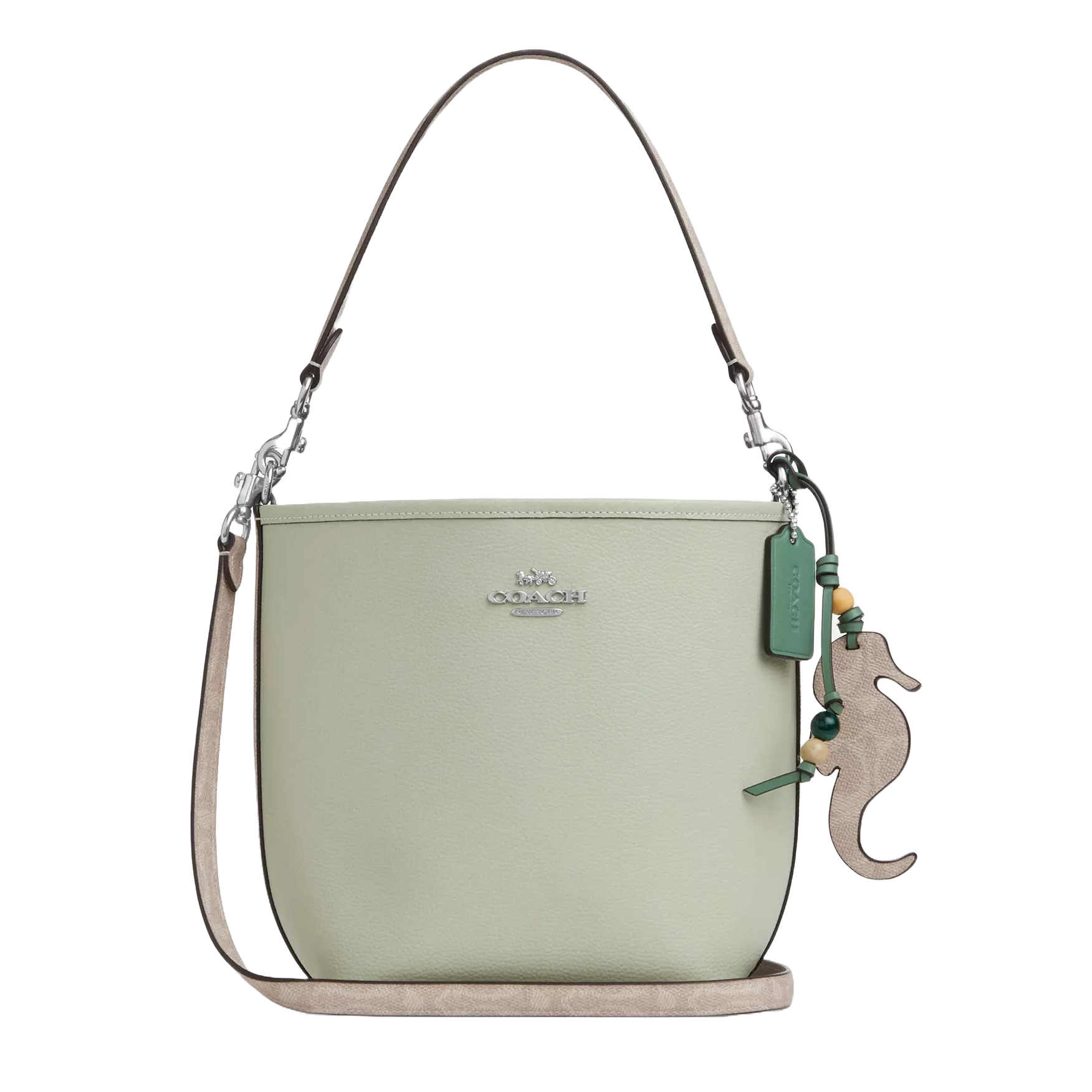 A light green Coach bucket bag with a detachable strap and seahorse charm, displaying the Coach logo on the front.