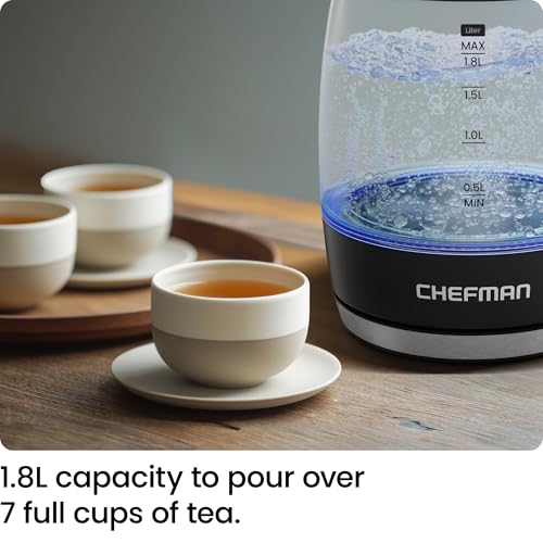 A Chefman rapid-boil electric kettle with a 1.8L capacity, clearly marked levels, and three filled tea cups on a wooden surface.