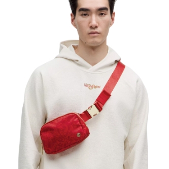 Red belt bag worn crossbody, featuring gold-tone hardware, embroidered details, and a compact design suitable for casual wear. Paired with a white hoodie.