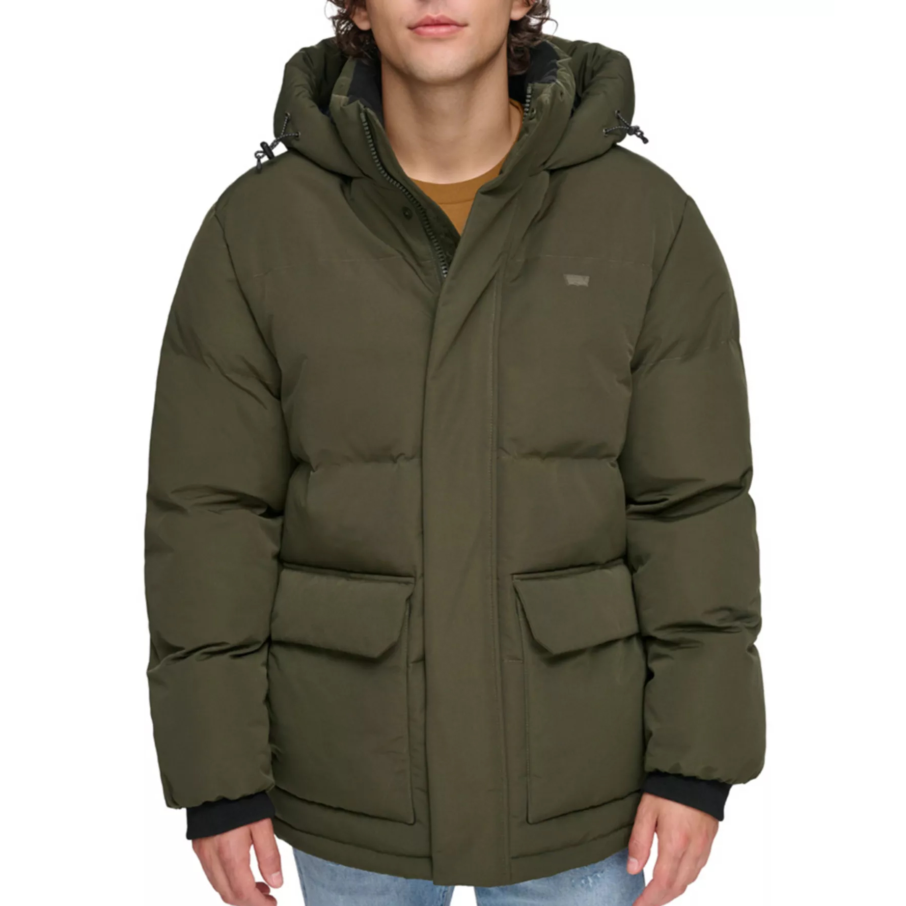 A person is wearing a green puffer jacket with a hood, featuring large front pockets. The jacket is paired with light blue jeans.