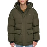 A person is wearing a green puffer jacket with a hood, featuring large front pockets. The jacket is paired with light blue jeans.