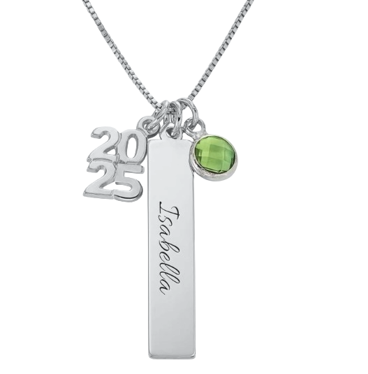 A silver necklace features three charms: the year \“2025,\“ a vertical bar with \“Isabella\“ inscribed, and a green gemstone pendant.