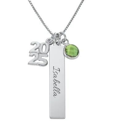 A silver necklace features three charms: the year \“2025,\“ a vertical bar with \“Isabella\“ inscribed, and a green gemstone pendant.