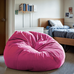 A large pink bean bag chair is situated in a cozy room with a bed and a bookshelf in the background.