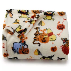 Cozy blanket featuring playful Halloween-themed characters from a popular children's series, with pumpkins and costumes on a soft, white fabric.