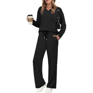 A woman is wearing a black long-sleeve top and pants set with a drawstring waist, holding a coffee cup. She has a black shoulder bag and is wearing white sneakers.