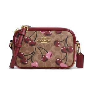 Coach Mini Jamie Camera Bag in cherry print features brown signature canvas with pink and red cherries, gold-tone hardware, a red leather strap, and a Coach tag.