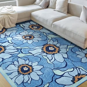 A large floral patterned area rug in shades of blue, with orange centers, is placed beneath a light beige sectional sofa with pillows, creating a cozy living room setting.