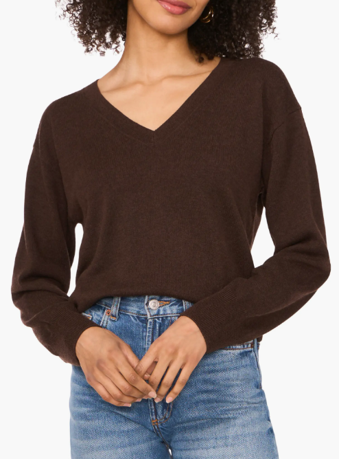 A woman is wearing a brown V-neck sweater paired with blue jeans.