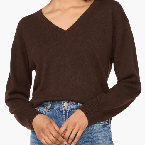 A woman is wearing a brown V-neck sweater paired with blue jeans.