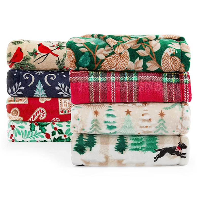 A stack of festive-themed blankets featuring various holiday patterns including cardinals, owls, plaid, candy canes, pine trees, and a black dog.