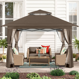 Outdoor patio gazebo with a brown canopy, mesh curtains, and a set of wicker furniture including a loveseat, two chairs, and a coffee table on a decorative rug. Surrounded by plants and shrubbery on a patio.