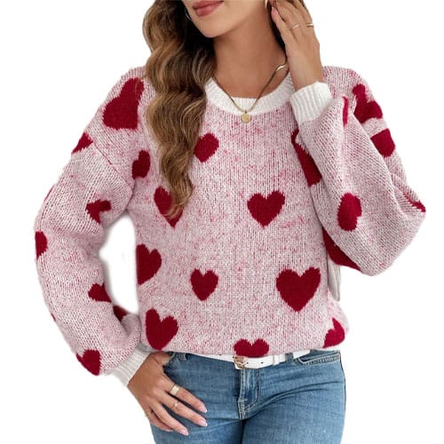 A woman is wearing a pink sweater with red heart patterns, paired with light blue jeans.