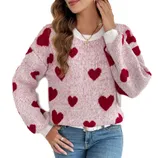 A woman is wearing a pink sweater with red heart patterns, paired with light blue jeans.