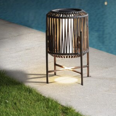 A cylindrical outdoor lantern with a wooden frame and metal stand, placed by a poolside.