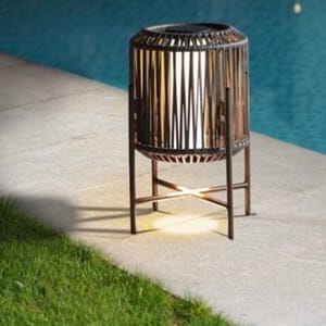 A cylindrical outdoor lantern with a wooden frame and metal stand, placed by a poolside.