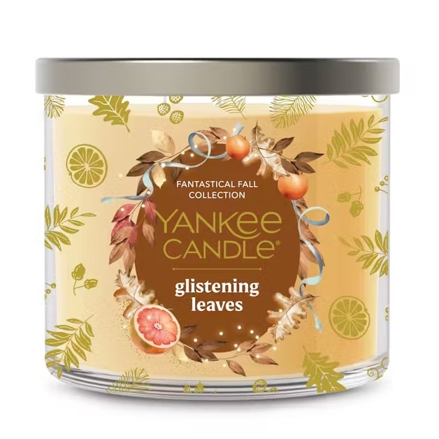Yankee Candle from the Fantastical Fall Collection, scent \“Glistening Leaves,\“ features a design with autumnal leaves, citrus, and small pumpkins.