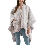 A person is wearing a plush, textured, light-colored poncho with wide sleeves and pockets, paired with light blue jeans.