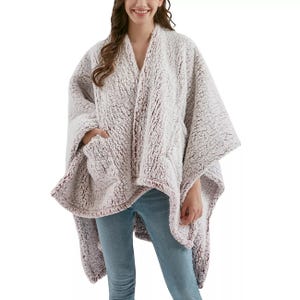 A person is wearing a plush, textured, light-colored poncho with wide sleeves and pockets, paired with light blue jeans.