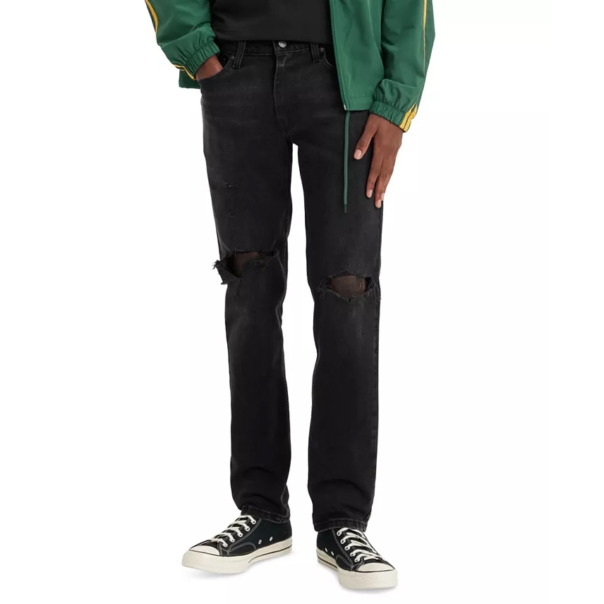 A person is wearing ripped black jeans paired with black and white sneakers and a green jacket with yellow stripes.