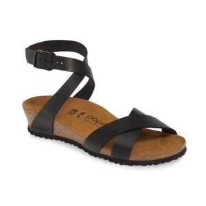A black sandal with an ankle strap, buckle closure, and cork wedge sole, marked \“Papillio.\“