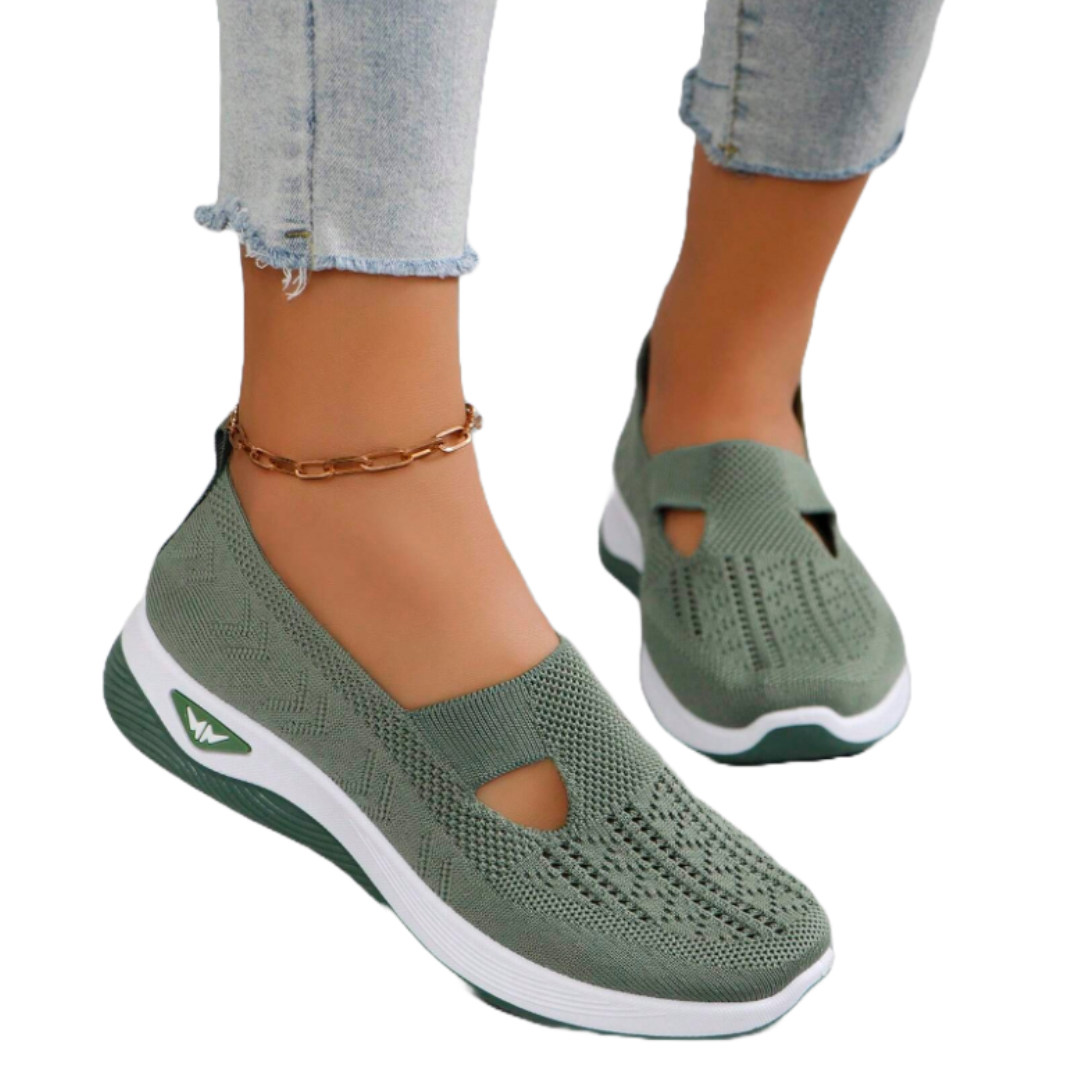 Green slip-on sneakers with a knit upper feature a breathable design and cutout details. They have a white and green cushioned sole for comfort, paired with light-wash denim jeans and a gold chain anklet.