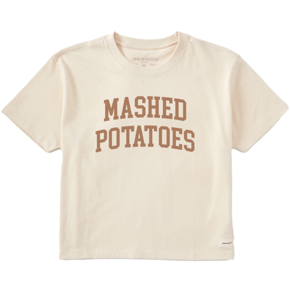 A cream-colored T-shirt with the words \“MASHED POTATOES\“ printed in brown, bold letters on the front.